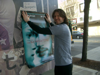 James Ritzman helping to hang a poster on a building while promotional modeling for 'The Butterfly Effect'.